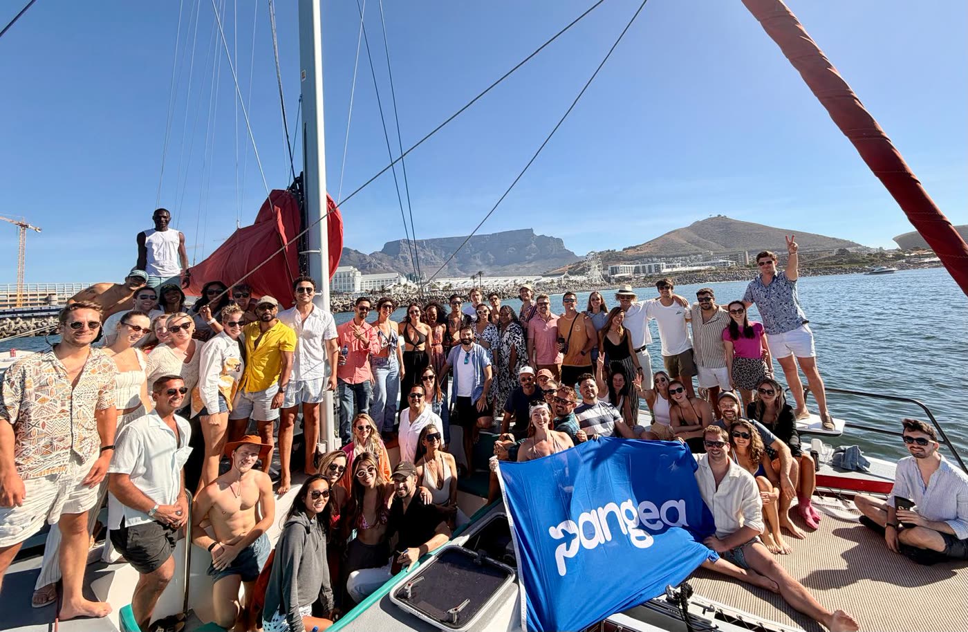 The Pangea community on a catamaran in Cape Town, Table Mountain behind them, holding a Pangea flag
